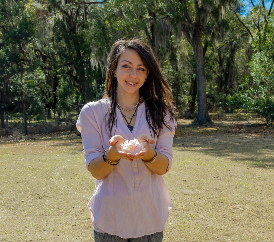 Erika, creator of Essentials Amora, holding a fresh blossom in the sun